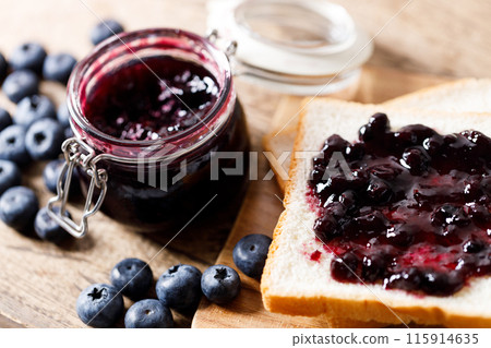 Blueberry jam with fresh berries on bread on rustic wooden table background. Selective focus. 115914635