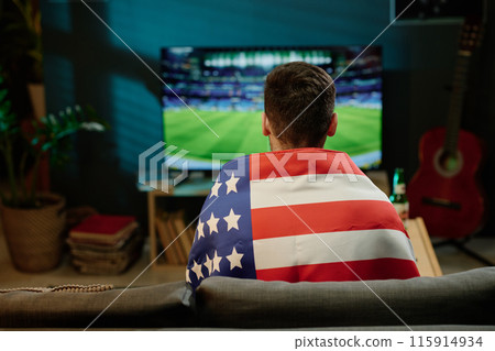 Rear view of unrecognizable man wearing flag sitting in living room watching sports event on TV at home Rear view of unrecognizable man wearing flag sitting in living room watching sports event on TV at home 115914934