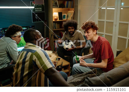 Multi-ethnic group of four young men sitting in living room discussing soccer match they watching on TV late in evening Multi-ethnic group of four young men sitting in living room discussing soccer match they watching on TV late in evening 115915101