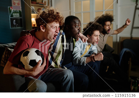 Multi-ethnic group of young male soccer fans sitting on couch in living room watching match on TV 115915136