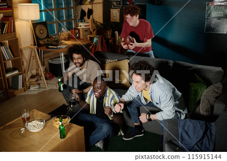Multi-ethnic group of young men spending evening indoors watching football match on TV, high angle view shot 115915144