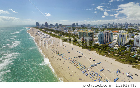 Travel destination in United States. South Beach sandy surface with tourists relaxing on hot Florida sun. Tourism infrastructure in southern USA. Miami Beach city with high luxury hotels and condos 115915483