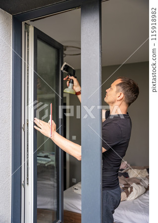 Young man cleans the windows in the house. He splashes detergent, rubs and removes water at the glass 115918982