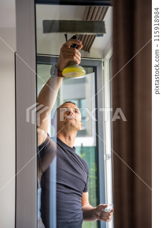 Young man cleans the windows in the house. He splashes detergent, rubs and removes water at the glass 115918984