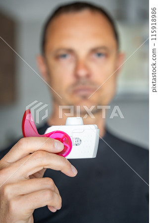 Close up view of man using medicine dry powder inhaler for treatment asthma or COPD diseases. Pharmaceutical product is used to treat lung inflammation and prevent asthma attack. Close up view of man using medicine dry powder inhaler for treatment asthma or COPD diseases. Pharmaceutical product is used to treat lung inflammation and prevent asthma attack. 115918986