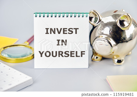 Invest in yourself symbol. Concept words INVEST IN YOURSELF on a blank sheet in a notebook in a composition with a piggy bank, magnifying glass, calculator, stickers on a gray background Invest in yourself symbol. Concept words INVEST IN YOURSELF on a blank sheet in a notebook in a composition with a piggy bank, magnifying glass, calculator, stickers on a gray background 115919481