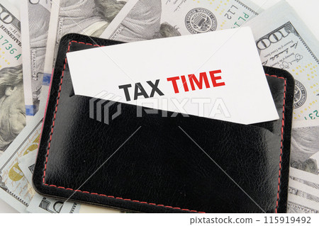 Business and tax concept. TAX TIME on a business card in a black leather accessory against the background of American dollars 115919492
