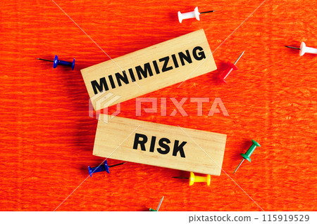 MINIMIZING RISK word written on wooden blocks with a hand on an orange background 115919529