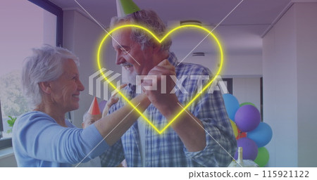 Yellow neon heart icon against caucasian senior couple dancing together during birthday party 115921122