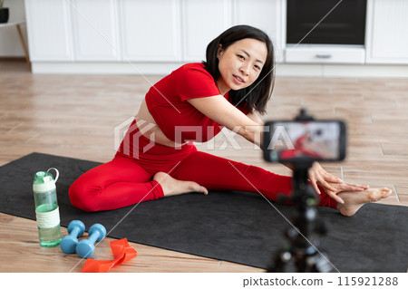 Woman filming online fitness tutorial stretching on yoga mat 115921288