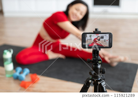 Woman filming virtual yoga class at home on smartphone 115921289