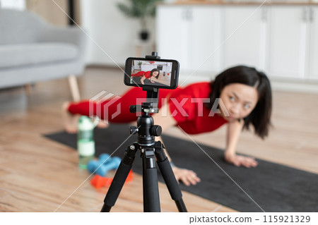 Woman recording fitness video doing push-ups at home 115921329