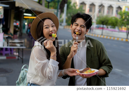 Asian couple traveler wearing a casual wear and hat in relationship buying a dessert snack on street food market in the evening. Backpacker traveling in Bangkok, Thailand.. Asian couple traveler wearing a casual wear and hat in relationship buying a dessert snack on street food market in the evening. Backpacker traveling in Bangkok, Thailand.. 115921692