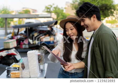 Asian couple traveler wearing a casual wear and hat in relationship buying a dessert snack on street food market in the evening. Backpacker traveling in Bangkok, Thailand.. 115921693