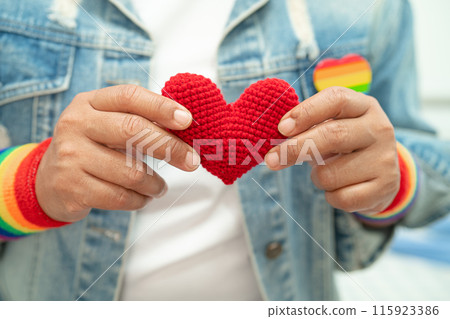 Asian lady wearing rainbow flag wristbands and hold red heart, symbol of LGBT pride month celebrate annual in June social of gay, lesbian, bisexual, transgender, human rights. 115923386