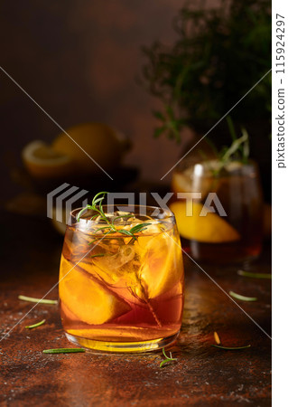 Iced tea or cocktail with ice, rosemary and lemon slices on the old brown table. 115924297