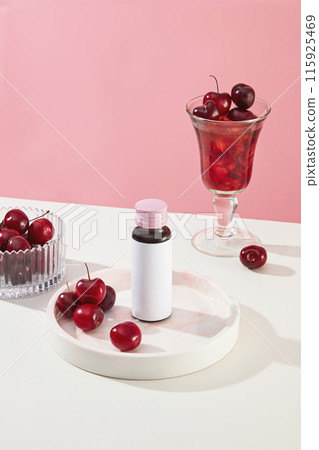 In the middle of the table displaying a white tray with a bottle of beauty supplement has cherry scent above, surrounded by a glass bowl of cherry and a cocktail glass of red liquid, space for text In the middle of the table displaying a white tray with a bottle of beauty supplement has cherry scent above, surrounded by a glass bowl of cherry and a cocktail glass of red liquid, space for text 115925469