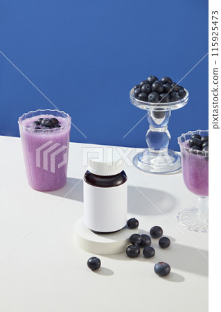 Mock up for advertising was taken from high angle, against the dark blue background. An unbranded bottle of beauty supplement, which extracted from blueberry, copy space for text Mock up for advertising was taken from high angle, against the dark blue background. An unbranded bottle of beauty supplement, which extracted from blueberry, copy space for text 115925473