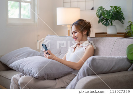 Young Woman Relax on Sofa and Engaging with Social Media on Smartphone in Cozy Living Room 115927239