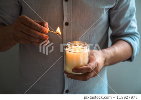 Man holding a burning candle in his hands, elegant young man with candle jar, meditation and mindfulness concept Man holding a burning candle in his hands, elegant young man with candle jar, meditation and mindfulness concept 115927973