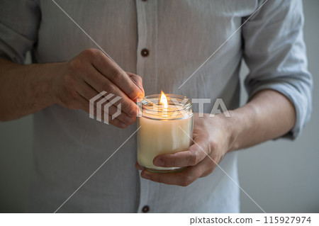 Man holding a burning candle in his hands, elegant young man with candle jar, meditation and mindfulness concept 115927974