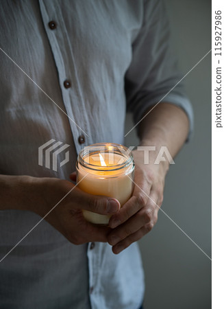 Man holding a burning candle in his hands, elegant young man with candle jar, meditation and mindfulness concept Man holding a burning candle in his hands, elegant young man with candle jar, meditation and mindfulness concept 115927986