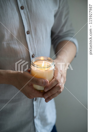 Man holding a burning candle in his hands, elegant young man with candle jar, meditation and mindfulness concept 115927987