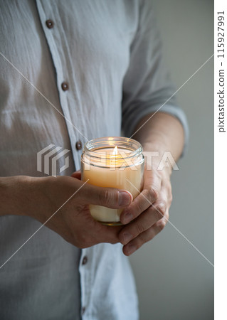 Man holding a burning candle in his hands, elegant young man with candle jar, meditation and mindfulness concept 115927991