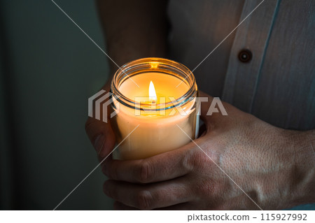 Man holding a burning candle in his hands, elegant young man with candle jar, meditation and mindfulness concept 115927992