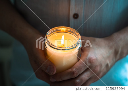 Man holding a burning candle in his hands, elegant young man with candle jar, meditation and mindfulness concept Man holding a burning candle in his hands, elegant young man with candle jar, meditation and mindfulness concept 115927994