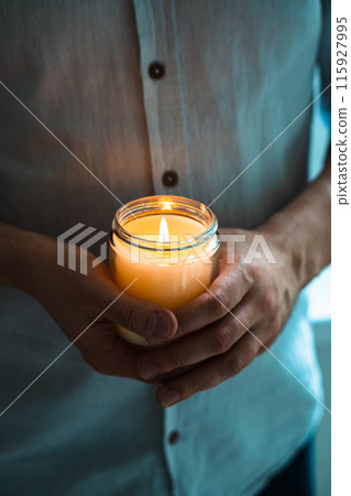 Man holding a burning candle in his hands, elegant young man with candle jar, meditation and mindfulness concept Man holding a burning candle in his hands, elegant young man with candle jar, meditation and mindfulness concept 115927995