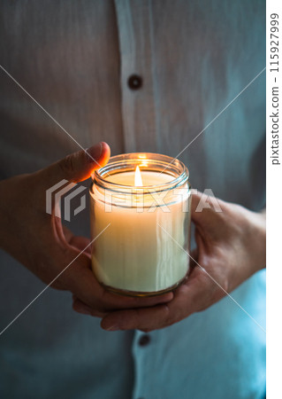 Man holding a burning candle in his hands, elegant young man with candle jar, meditation and mindfulness concept 115927999