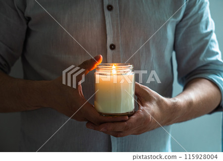 Man holding a burning candle in his hands, elegant young man with candle jar, meditation and mindfulness concept Man holding a burning candle in his hands, elegant young man with candle jar, meditation and mindfulness concept 115928004
