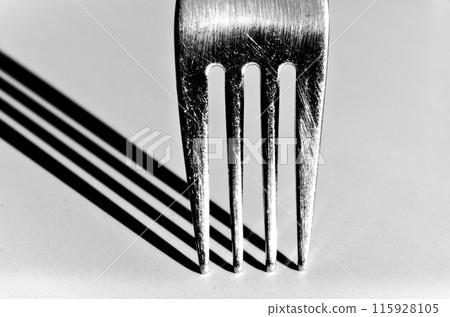 Closeup of a fork vertically on a white surface, with a harsh shadow Closeup of a fork vertically on a white surface, with a harsh shadow 115928105
