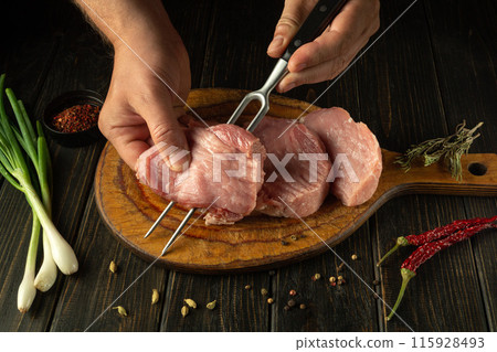 Cooking steak meat by hands of chef for barbecue. Raw veal meat on kitchen vintage table with spices and onions Cooking steak meat by hands of chef for barbecue. Raw veal meat on kitchen vintage table with spices and onions 115928493