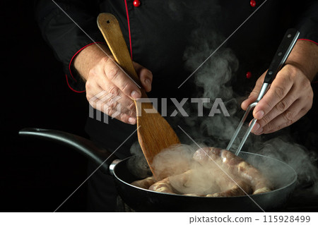 Chef cooks meat sausage in a frying pan. Low key concept of cooking sausage in a tavern or cook room kitchen 115928499
