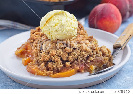 Peach Crisp or cobbler on plate with scoop of vanilla ice cream, horizontal 115928940