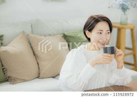 Middle-aged woman drinking coffee in the living room Middle-aged woman drinking coffee in the living room 115928972