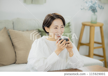 Middle-aged woman drinking coffee in the living room Middle-aged woman drinking coffee in the living room 115929001