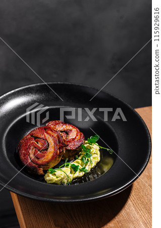 Gourmet bacon-wrapped meat and vegetables on black plate 115929616