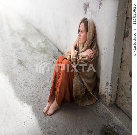 A girl in poor clothes sits on the ground A girl in poor clothes sits on the ground 115929629