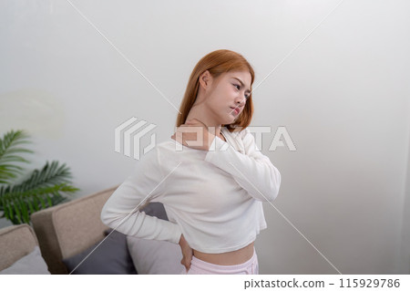 Woman Experiencing Neck and Back Pain at Home, Demonstrating Discomfort and Ache in a Modern Living Space Woman Experiencing Neck and Back Pain at Home, Demonstrating Discomfort and Ache in a Modern Living Space 115929786