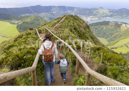 A woman and a child are walking on a path in a lush green area A woman and a child are walking on a path in a lush green area 115932621