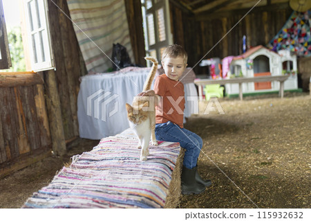 A boy sits on a hay bale next to a cat A boy sits on a hay bale next to a cat 115932632