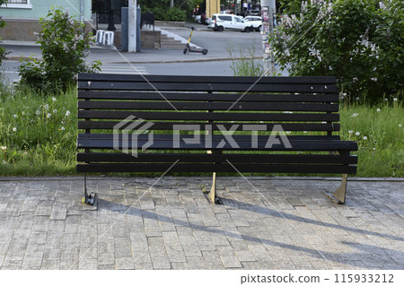 A black wooden bench in the city in the evening. A place to relax in the park. A black wooden bench in the city in the evening. A place to relax in the park. 115933212
