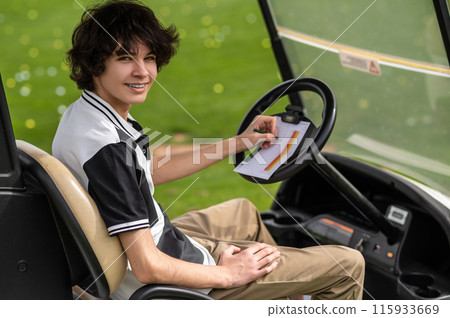 Dark-haired guy sitting in a vehicle on a golf field 115933669