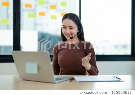 Smiling Call Center Agent with Headset Working on Laptop in Modern Office with Sticky Notes on Glass Wall Smiling Call Center Agent with Headset Working on Laptop in Modern Office with Sticky Notes on Glass Wall 115933682