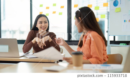 Two Young Women Collaborating in a Modern Office Setting with Laptops and Documents Two Young Women Collaborating in a Modern Office Setting with Laptops and Documents 115933718