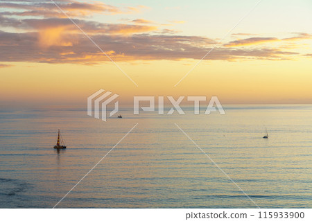 Sailboat peacefully drifting on ocean under beautiful sunset sky Sailboat peacefully drifting on ocean under beautiful sunset sky 115933900