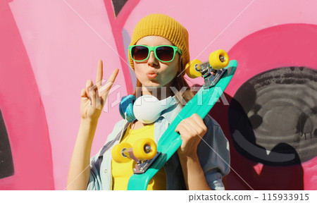 Stylish modern young teenager girl with skateboard in glasses, listening to music on graffiti wall 115933915